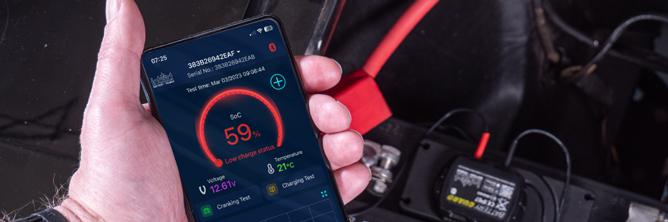 The picture shows a smartphone in front of a battery. The battery charge status is checked in the Battery-Guard app.